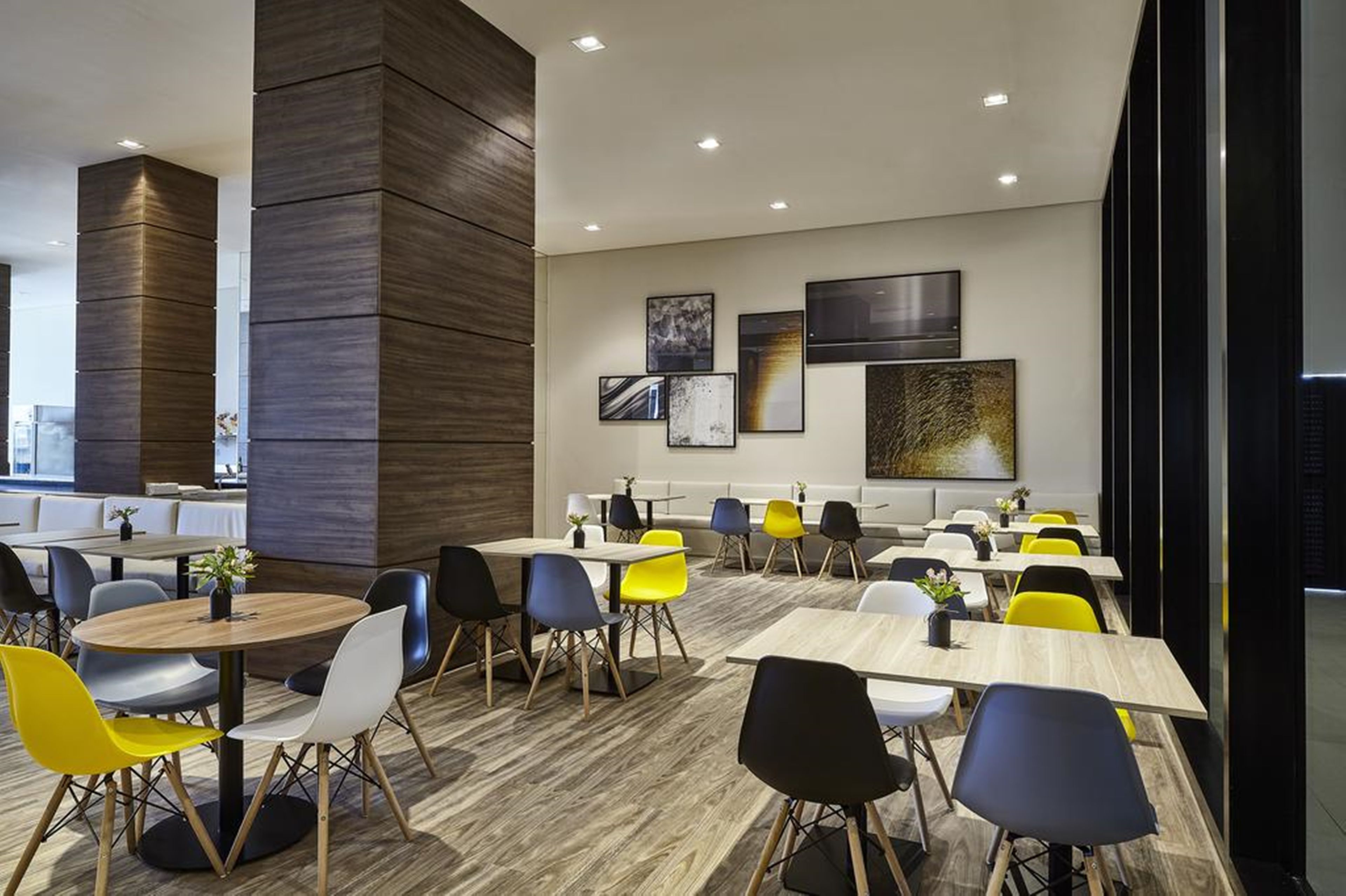 Un comedor moderno con mesas redondas y sillas coloridas, un muro decorativo de madera y obras de arte en las paredes.
