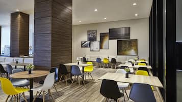 Un comedor moderno con mesas redondas y sillas coloridas, un muro decorativo de madera y obras de arte en las paredes.