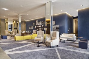 A modern lobby with a geometric carpet design, contemporary seating arrangements, and a large mirror reflecting the space. - Contemporaneo (Campinas)