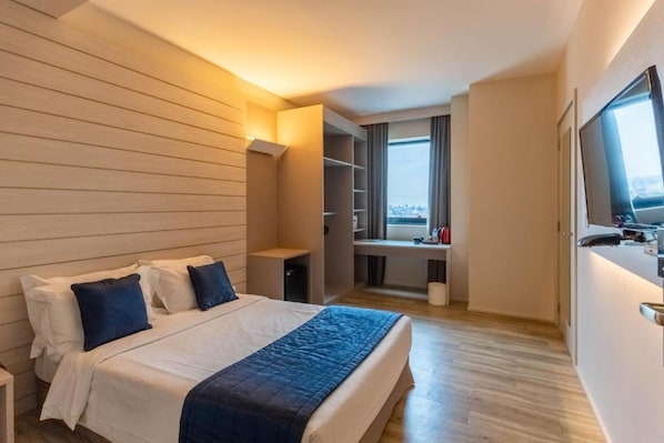 Una habitación de hotel con cama, escritorio, armario y ventana con vista a la ciudad.