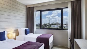Habitación de hotel con dos camas, un escritorio y un ventanal grande con vistas a la ciudad.