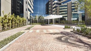 A modern building with a glass facade, a brick pathway, and a white pergola structure. - Contemporaneo (Campinas)