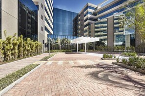 A modern building with a glass facade, a brick pathway, and a white pergola structure. - Contemporaneo (Campinas)