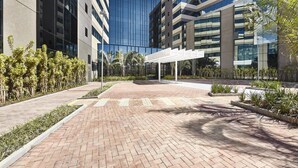 A modern building with a glass facade, a brick pathway, and a white pergola structure. - Contemporaneo (Campinas)