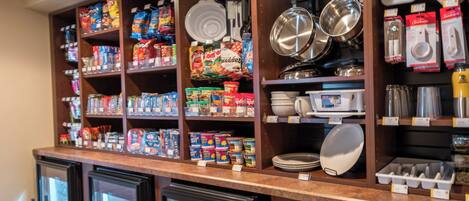 A kitchen area with shelves stocked with food items, pots, pans, and kitchenware.