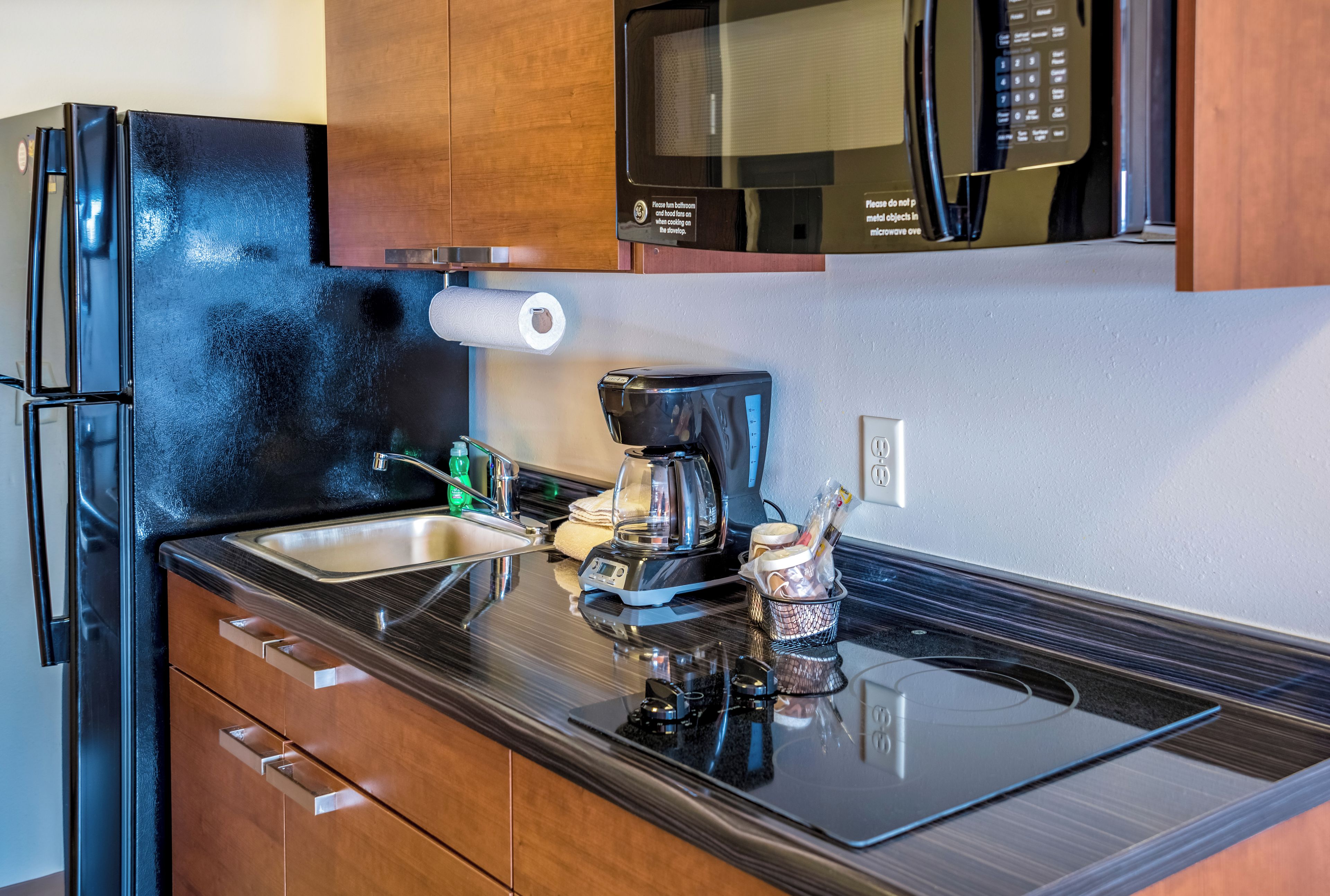 Una cucina con un frigorifero nero, un forno a microonde, una macchina per il caffè e un lavello.