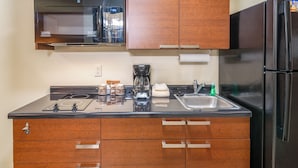A kitchen with wooden cabinets, a black refrigerator, a microwave, a coffee maker, and a sink. - My Place Hotel-marquette, MI (Marquette)