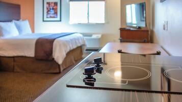 Une chambre d’hôtel moderne équipée d’un lit, d’un téléviseur à écran plat, d’une petite table et d’une plaque de cuisson intégrée.