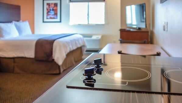 Una habitación de hotel moderna con cama, televisor de pantalla plana, una mesita y estufa integrada.