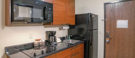 Una cocina compacta con microondas, cafetera, refrigerador y armarios de madera.