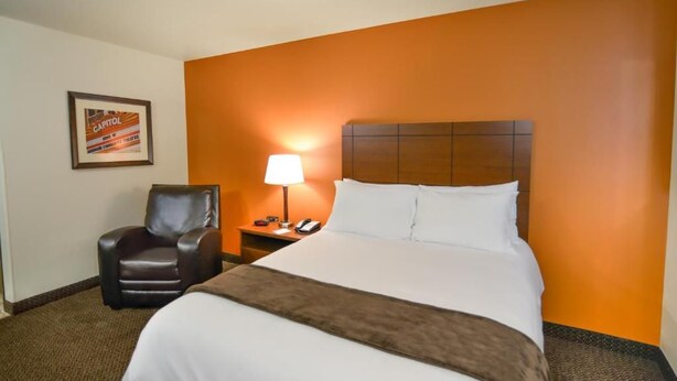 A hotel room with a large bed, a chair, a nightstand with a lamp, and a framed picture on the wall. - My Place Hotel-marquette, MI (Marquette)