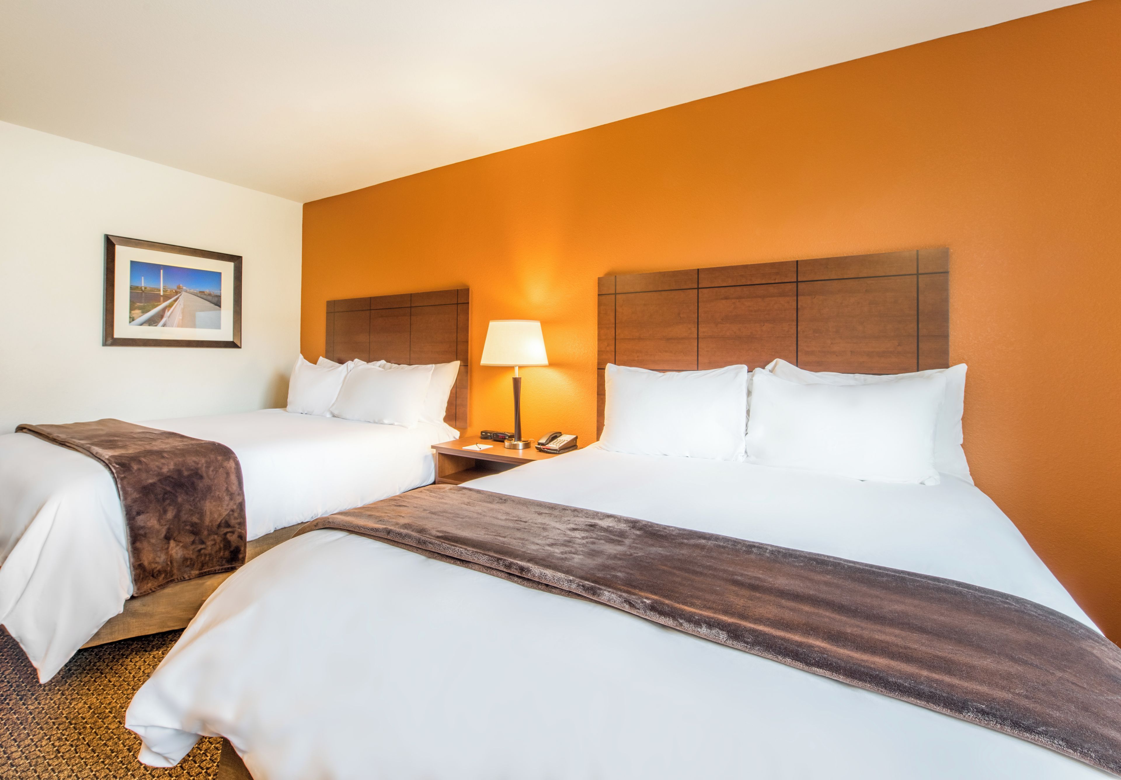 A hotel room with two beds, a nightstand with a lamp, and a framed picture on the wall.