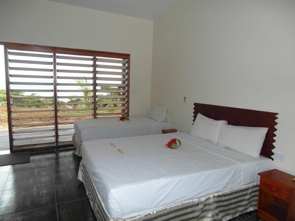 A bedroom with two beds, a wooden headboard, a nightstand, and a view through a window with blinds. - Funky Fish Beach Resort (Malolo Island)