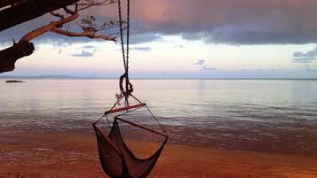 A hammock hanging from a wooden structure over a beach with calm water and a cloudy sky.