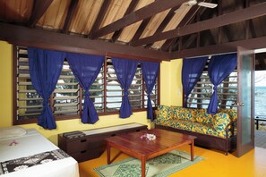 A room with a bed, a wooden bench, a sofa, and a table. There are windows with curtains, and a view of the sea is visible through the windows. - Funky Fish Beach Resort (Malolo Island)