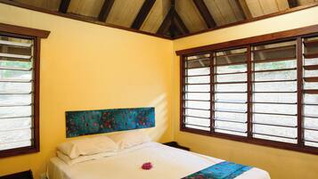 Una habitación con cama, techo de madera y ventanas con rejas.