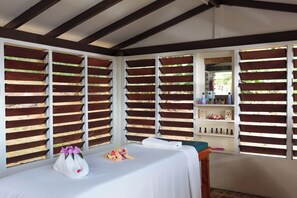 A room with a bed, a towel, and a bouquet of flowers. There are wooden slats on the windows and a shelf with bottles. - Funky Fish Beach Resort (Malolo Island)