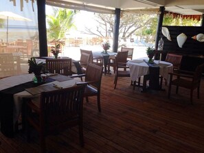 An outdoor dining area with wooden tables and chairs, potted plants, and a view of the beach. - Funky Fish Beach Resort (Malolo Island)