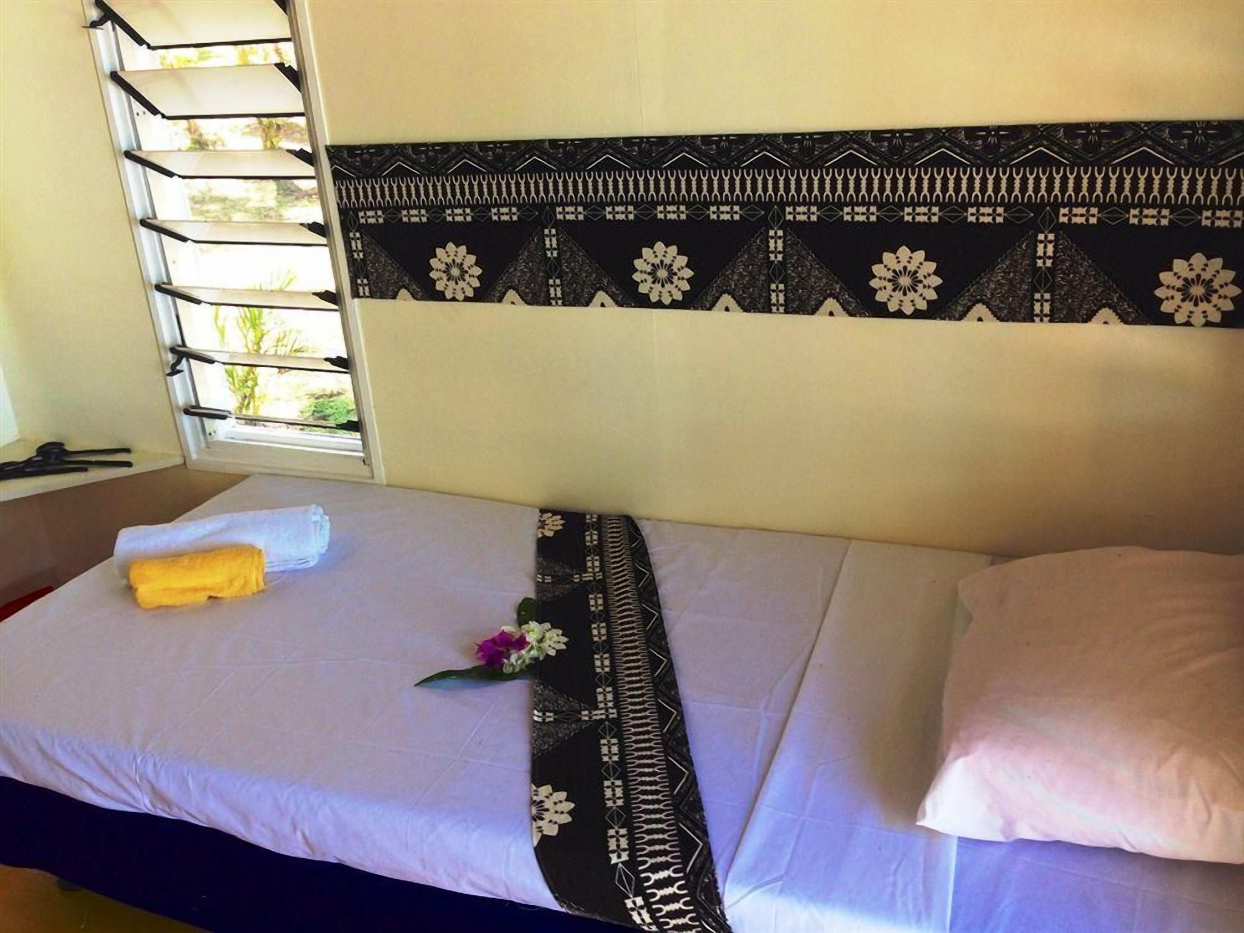A single bed with a patterned headboard, a window with blinds, and a towel on the bed.