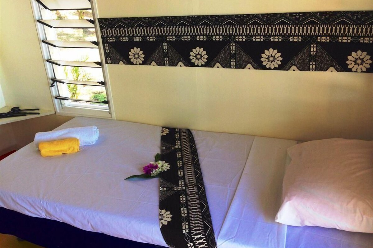A single bed with a patterned headboard, a window with blinds, and a towel on the bed.