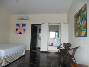 Een kamer met een bed, een stoel, een tafel, een koelkast en een deur die naar een keuken leidt.