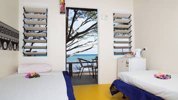 A room with two beds, a desk, and a view of the beach through a door.