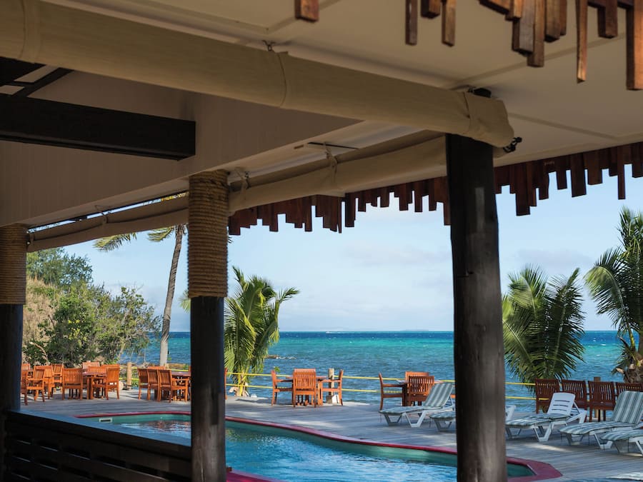 Une terrasse en bois avec des chaises longues et une piscine, offrant une vue sur l’océan.