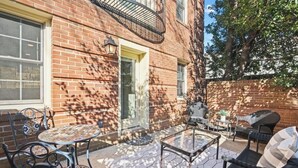 Une terrasse avec un mur en briques, une porte et une fenêtre. On y trouve des chaises et une table d’extérieur.