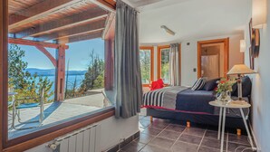 Ein Schlafzimmer mit Bett, kleinem Tisch, Lampe und Blick ins Freie.