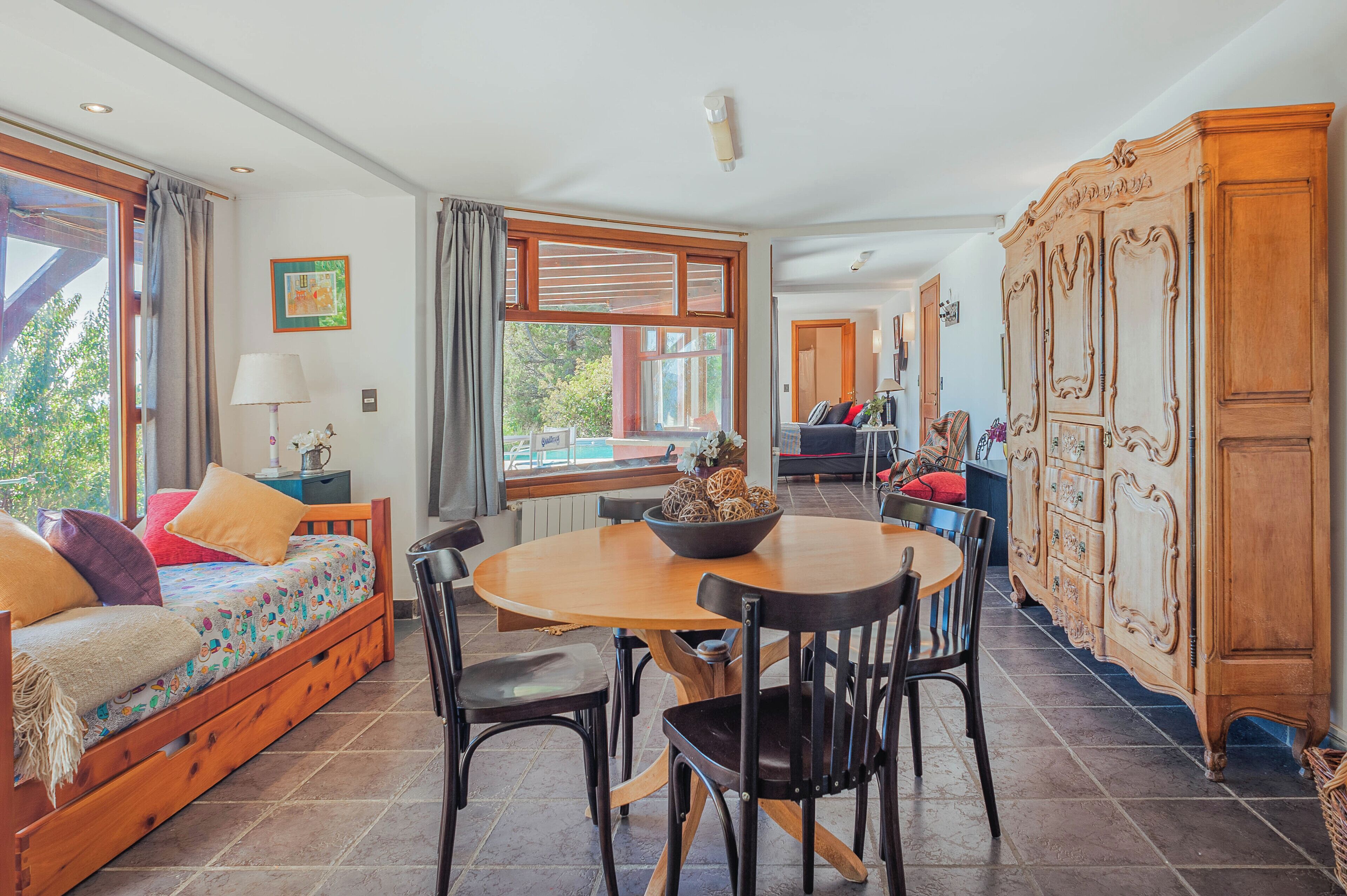 Una habitación acogedora con cama, una mesa de comedor con sillas, un aparador de madera y un ventanal grande.