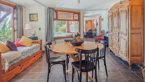 Ein gemütliches Zimmer mit einem Bett, einem Esstisch mit Stühlen, einem Holzschrank und einem großen Fenster.