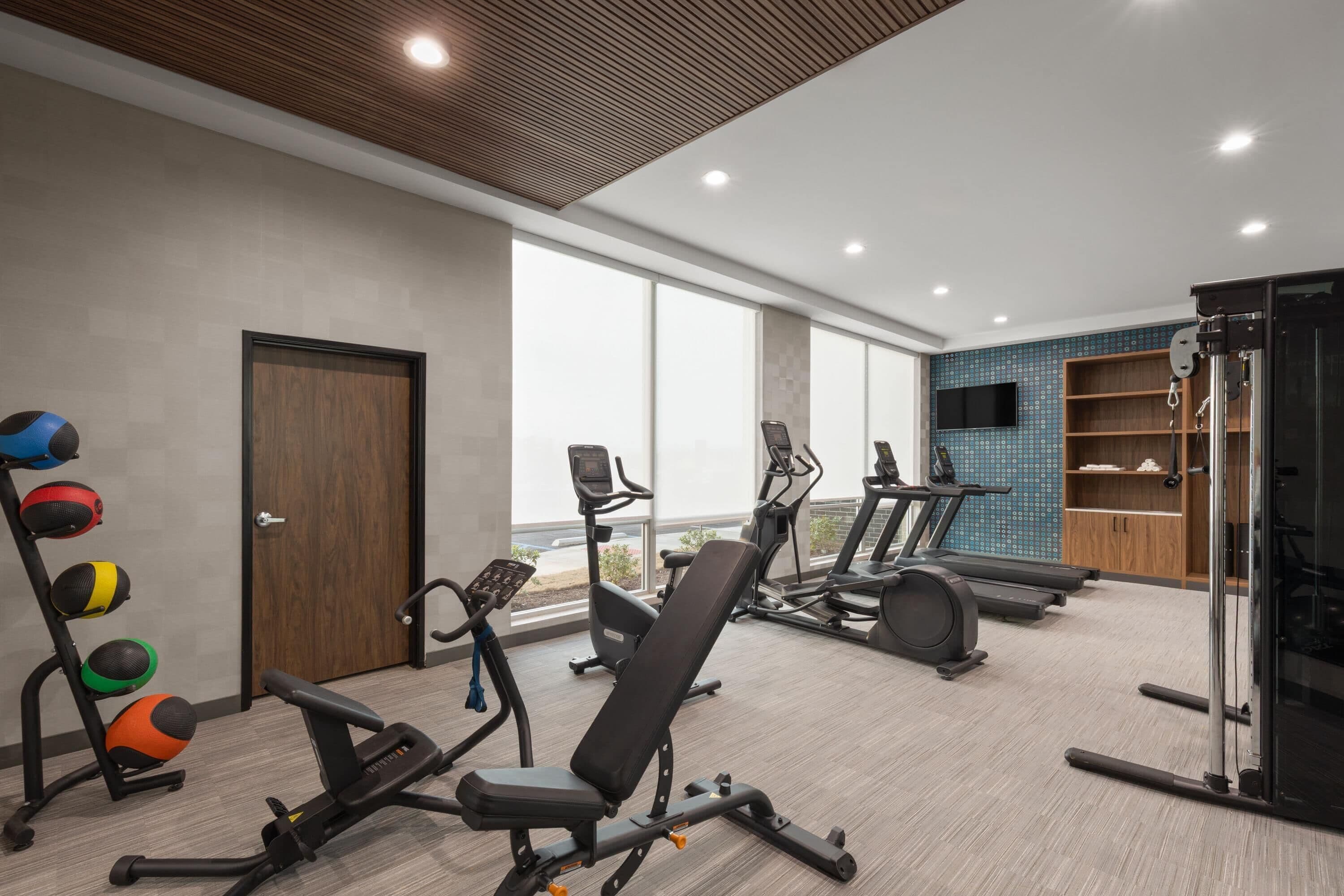 A gym with exercise equipment, a bench, and a wall-mounted TV.