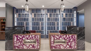 A reception desk with a marble top and a geometric pattern, two chairs, a blue wall with a grid pattern, and a wooden shelf with items. - La Quinta Inn & Suites by Wyndham Athens I-65 (Athens)