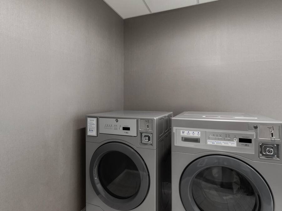 Zwei Waschmaschinen mit Frontlader in einer Ecke, an einer schlichten Wand.