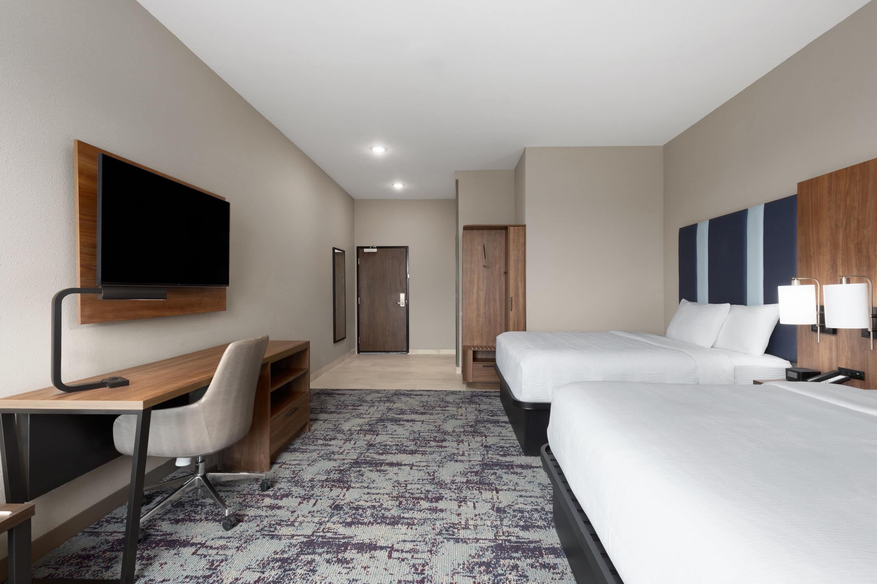 A hotel room with a bed, a desk, a chair, a TV, and a wardrobe.