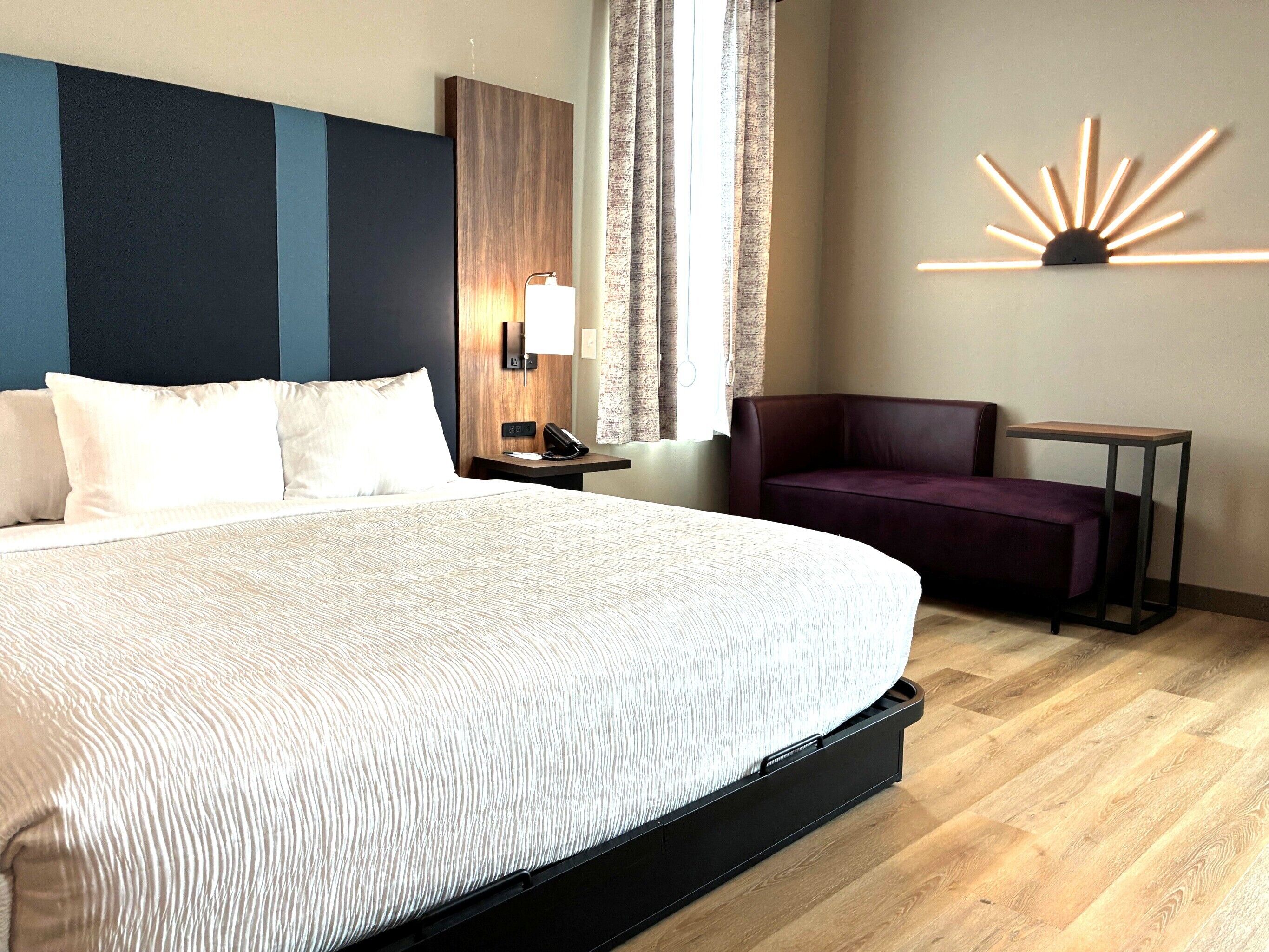 Habitación de hotel con una cama grande, un escritorio, una silla, una mesita de noche, una lámpara y una lámpara de pared.