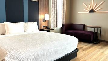 Habitación de hotel con una cama grande, un escritorio, una silla, una mesita de noche, una lámpara y una lámpara de pared.