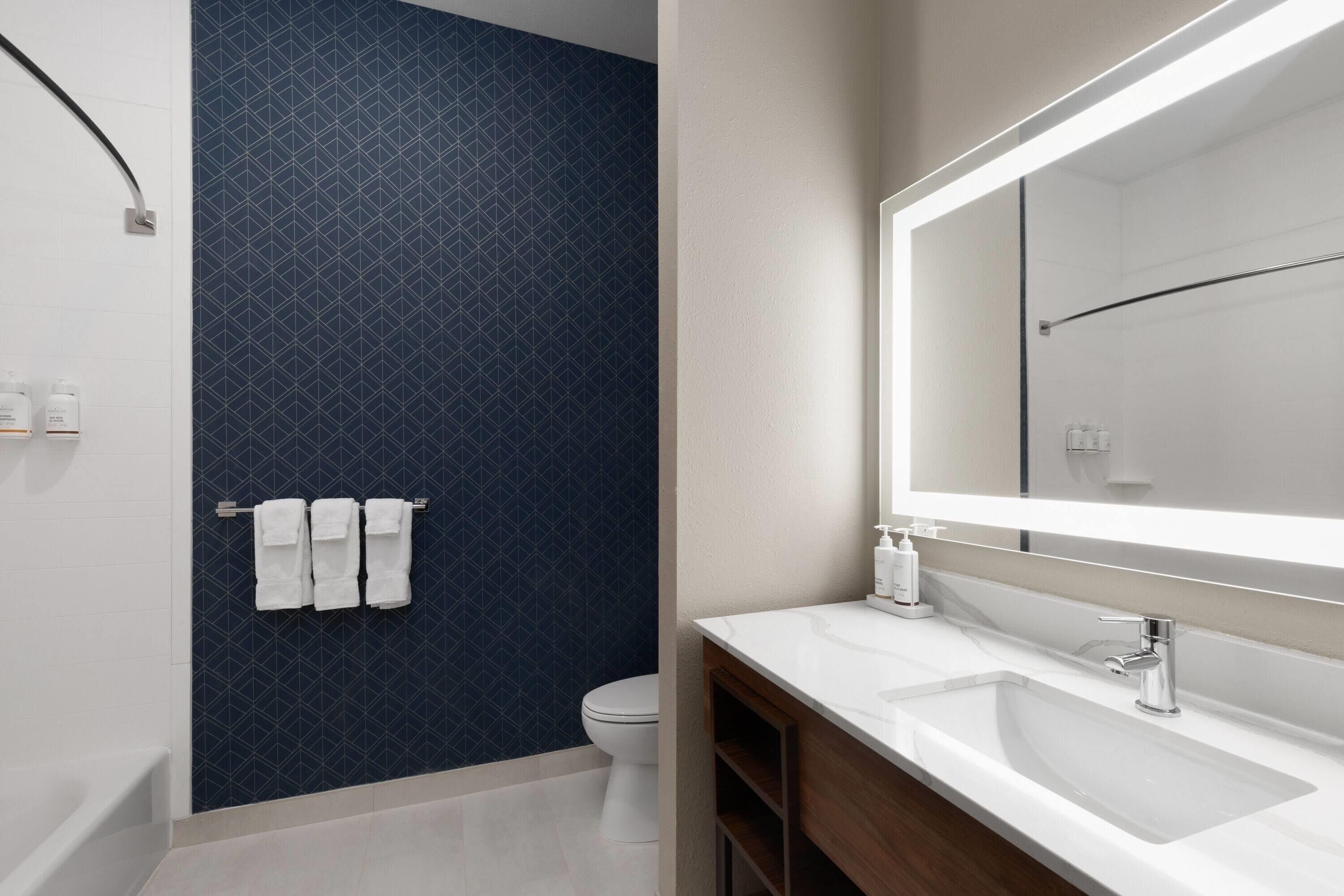 A modern bathroom with a white sink, a large mirror, and a dark blue tiled wall.