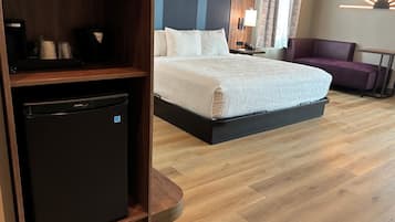 Habitación de hotel con cama, escritorio con computadora, refrigerador pequeño, silla y lámpara.