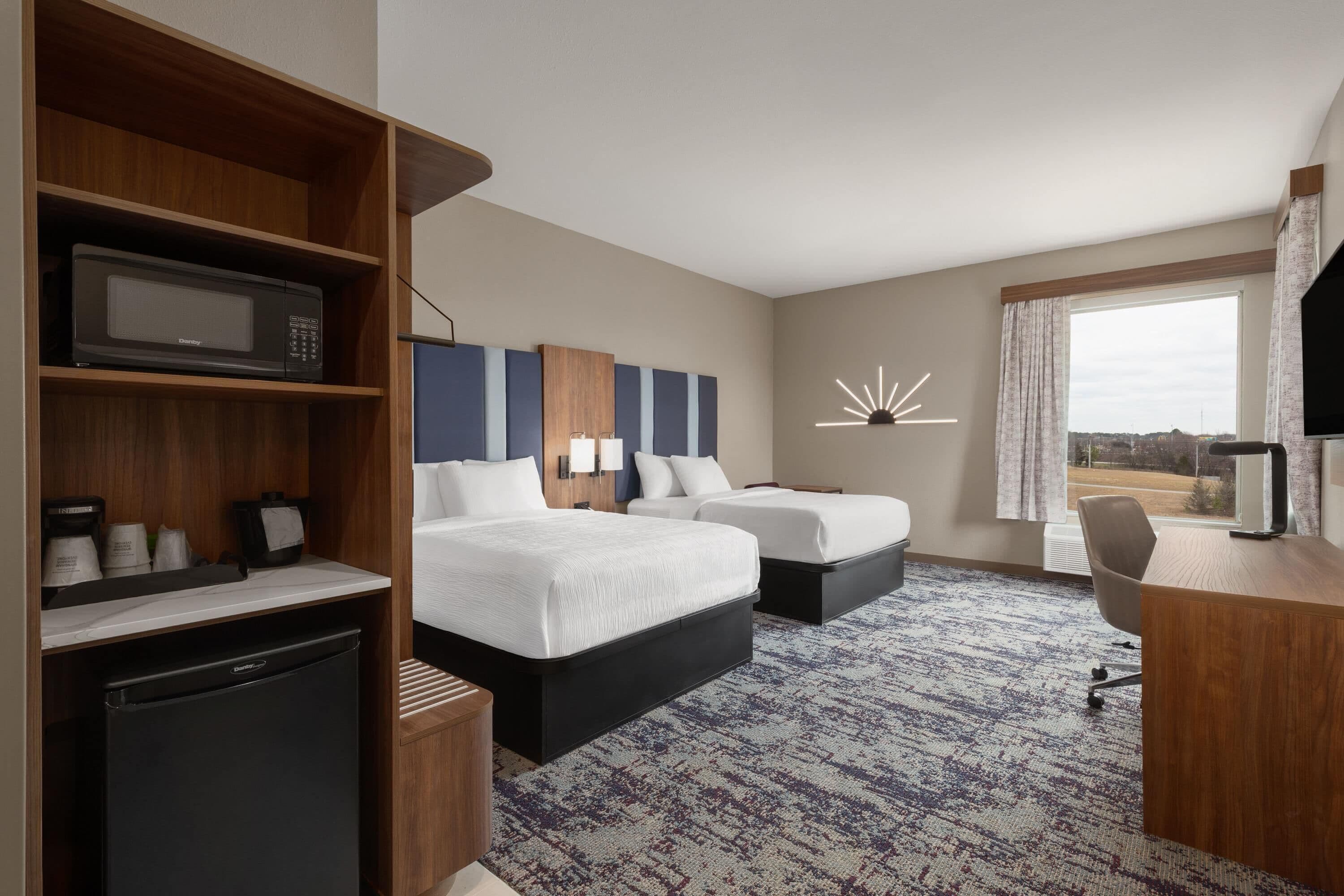 Une chambre d’hôtel avec deux lits, un bureau, un four à micro-ondes, un réfrigérateur et une grande fenêtre donnant sur un beau paysage.