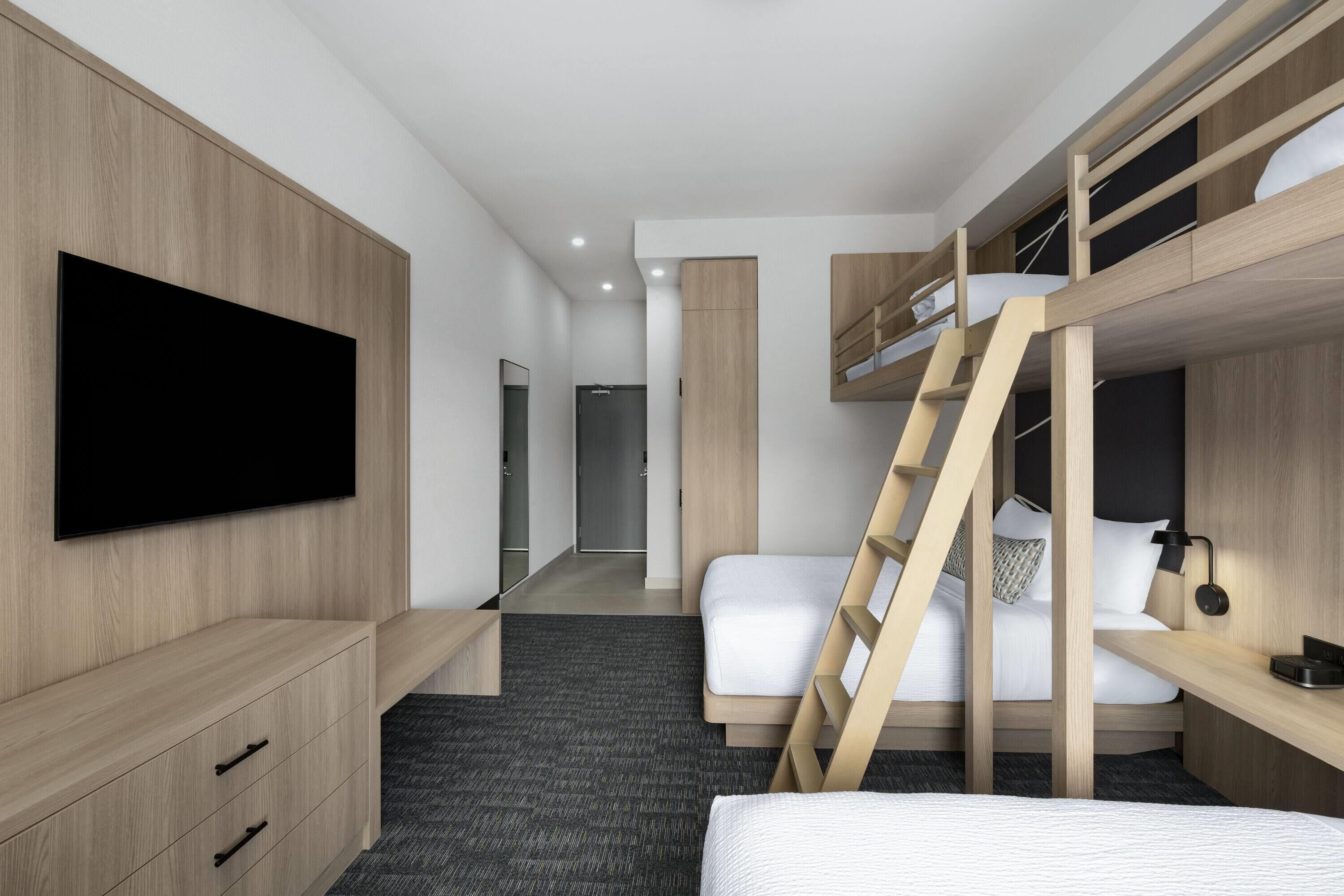 Habitació d'hotel moderna amb lliteres, televisió de pantalla plana, escriptori i armari.