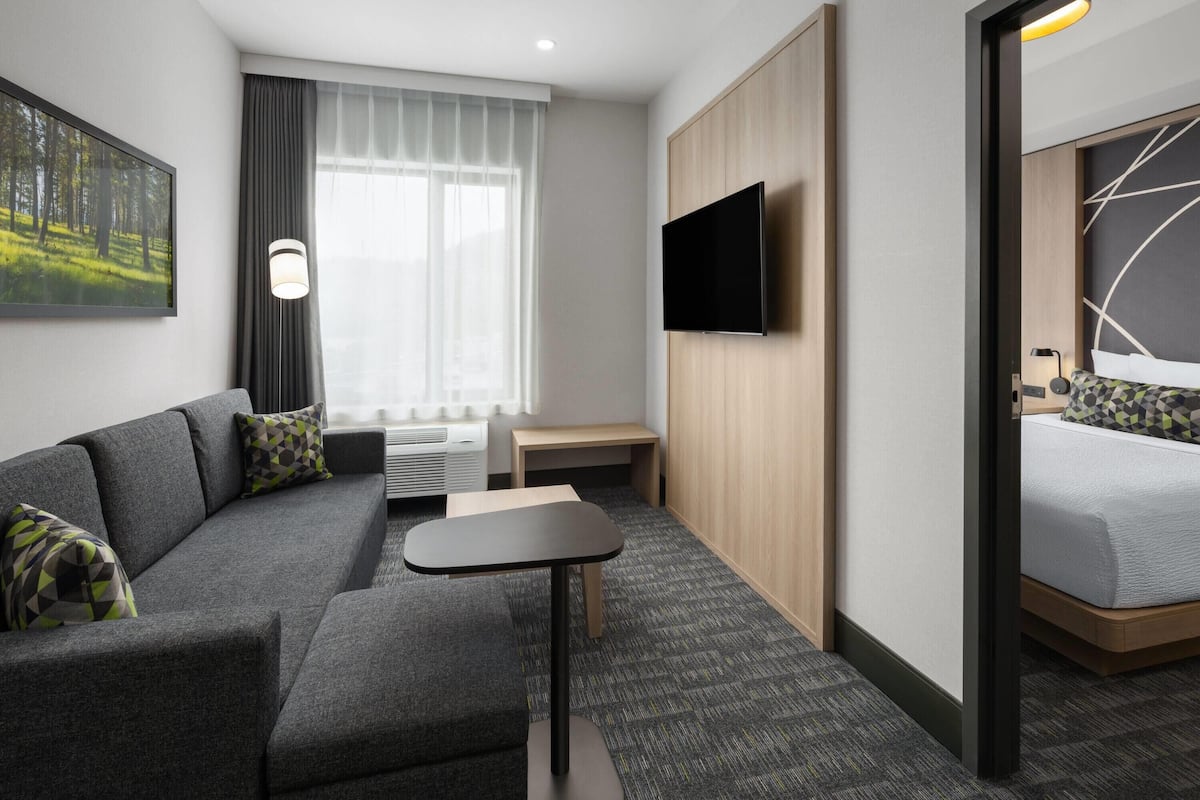 Una habitación de hotel moderna con sofá, una mesita, televisor, cama y ventana con cortinas.