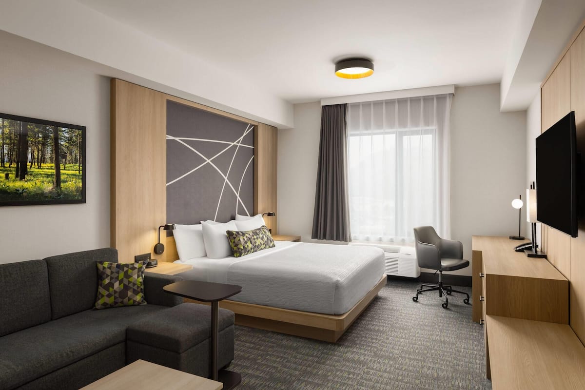 Una habitación de hotel moderna con una cama, un sofá, un escritorio, un televisor y un ventanal grande.