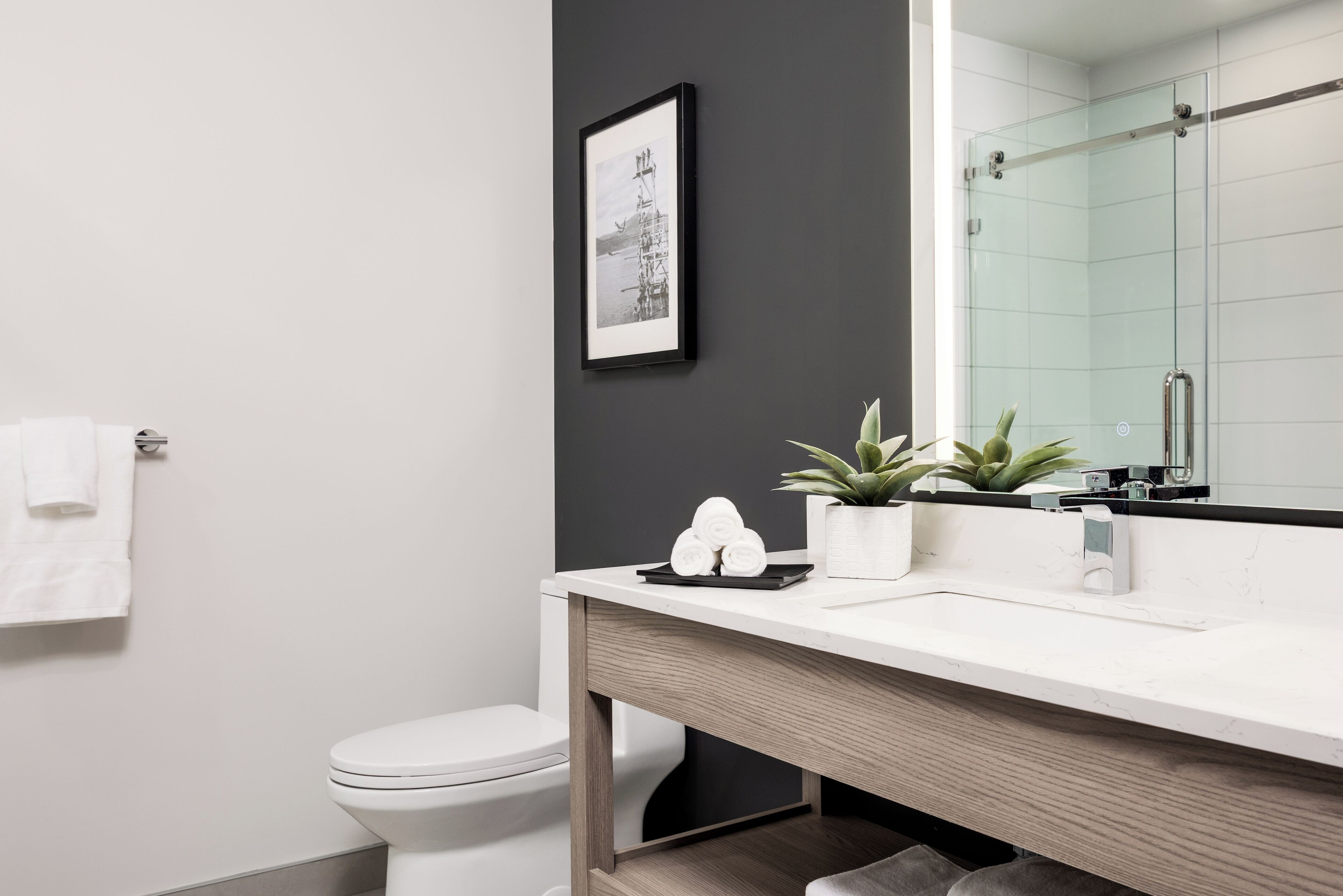 Ein modernes Badezimmer mit Toilette, Holzwaschtisch, Spiegel und einem gerahmten Bild an der Wand.