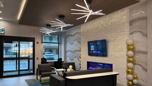 A modern reception area with a black reception desk, a mounted TV, and a wall-mounted screen displaying information. - La Quinta Inn & Suites By Wyndham Kelowna Bc (Kelowna)