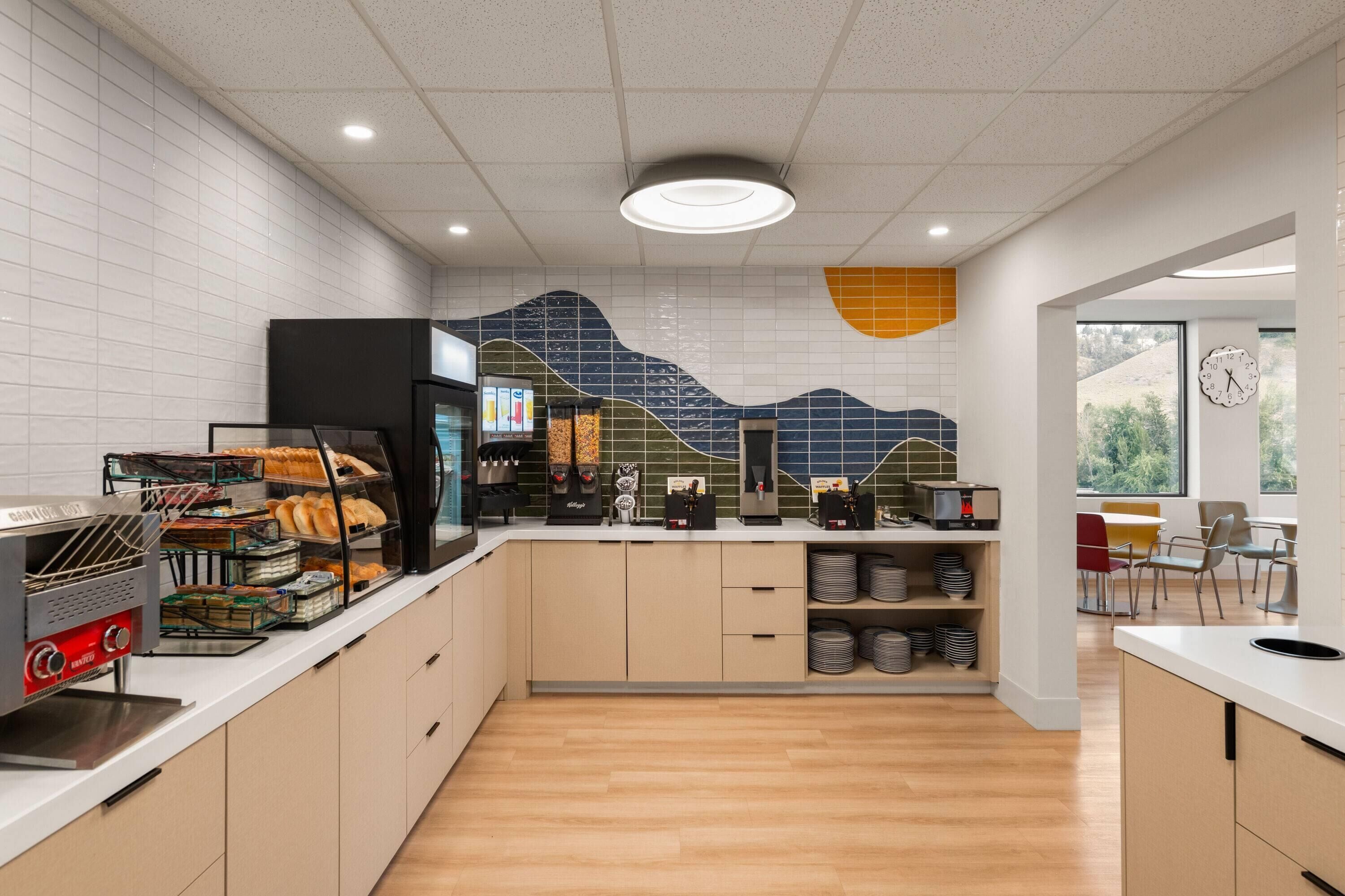 Une cuisine moderne équipée d’un four à micro-ondes, d’un grille-pain et d  ’une machine à café. On y trouve des étagères avec de l’assiette et une horloge au mur.