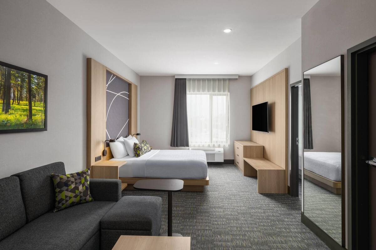 Ein modernes Hotelzimmer mit Bett, Sofa, Fernseher und einem großen Fenster.