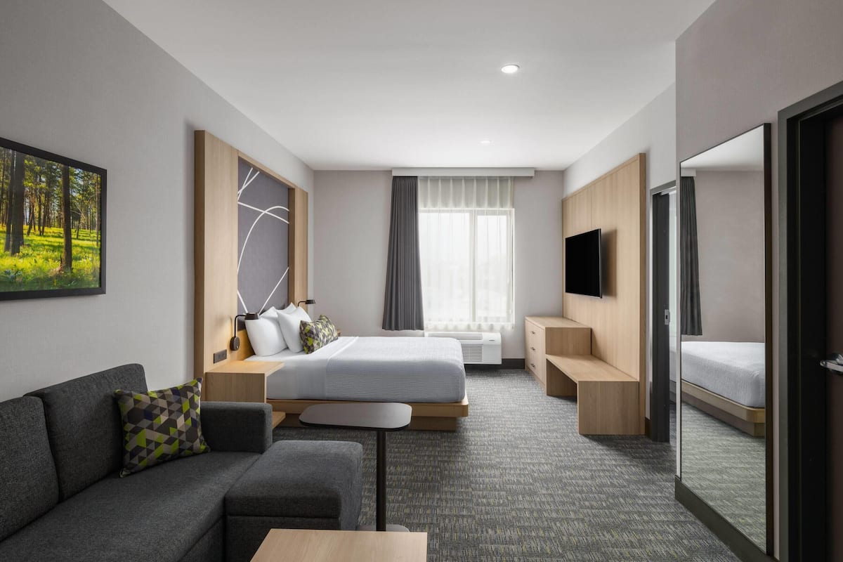 Una habitación de hotel moderna con cama, sofá, televisor y un ventanal grande.