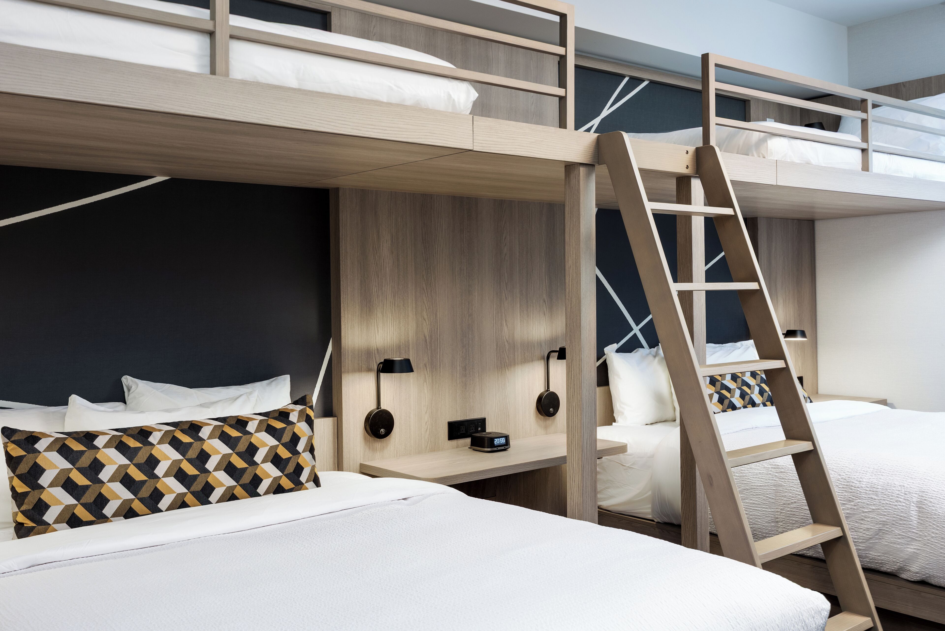 Una camera con un letto a castello, una scala in legno, un comodino con una lampada e un cuscino decorato.