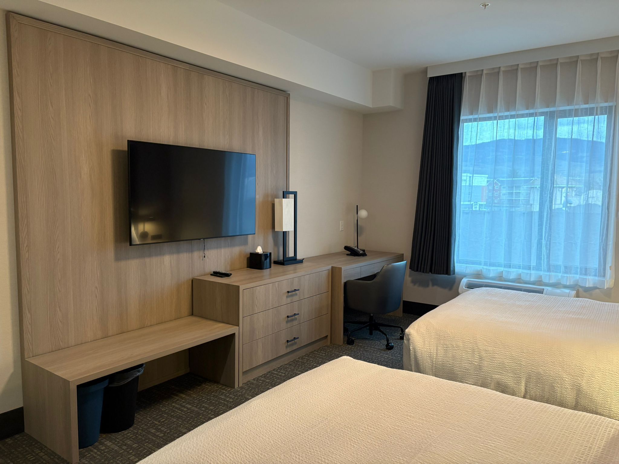 A hotel room with two beds, a desk with a chair, a television, and a window with curtains.